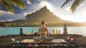 Personne en méditation yoga face au lagon turquoise de Raiatea avec la montagne sacrée en arrière-plan, entourée d'éléments traditionnels polynésiens et de fleurs tropicales dans une atmosphère mystique